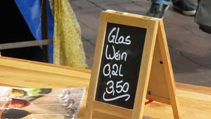 Auf einem Tisch steht eine kleine Kreidetafel mit der Aufschrift "Glas Wein. 0,2 Liter. 3,50 Euro."
