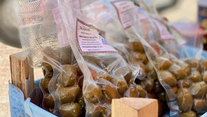 Durchsichtige Kunststoffbeutel mit eingeschweiten grnen Oliven stehen auf einem Verkaufstresen.